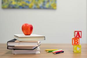 Apple on a pile of books with colored pencils and blocks to the side.